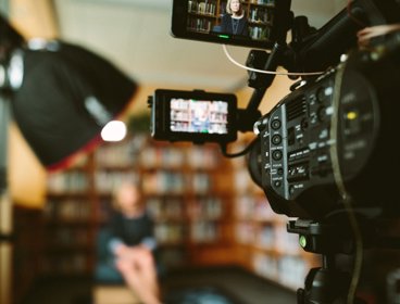 Camera filming person sat on a chair in front of bookcases