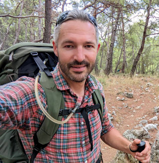 Tom Allen in hiking gear on an unpaved road in a forest.