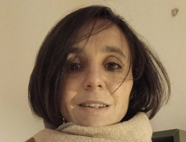 Person wearing a multicolored scarf wrapped around their neck and a purple jumper indoors.