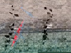 A red kayak in crystal clear blue water seen from above.