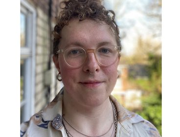 Person wearing a patterned button-up shirt standing outdoors near a brick wall.