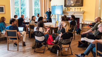 A presenter stands next to a screen with a presentation while listening attentively to an audience member talking.