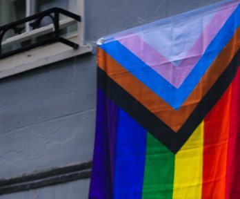 The LGBTQ+ flag hanging outside a window.
